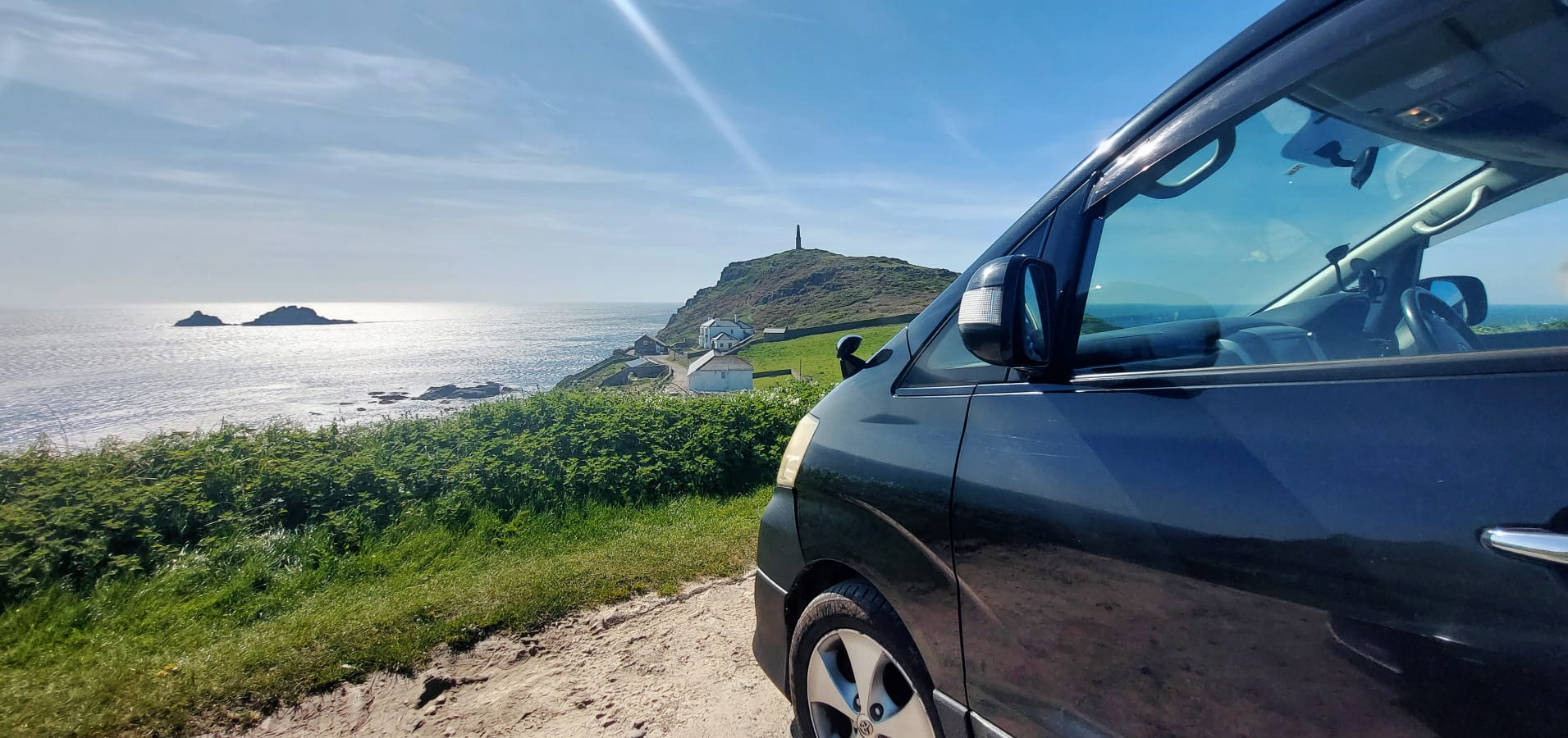 An image of Frida Go's multi person licensed private hire taxi parked in the sunshine by the seaside at Cape Cornwall near St Just in Cornwall