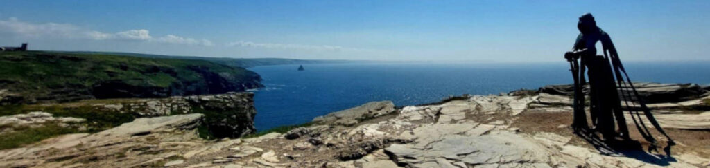 a metal statue on a headland above deep blue sea at Tintagel