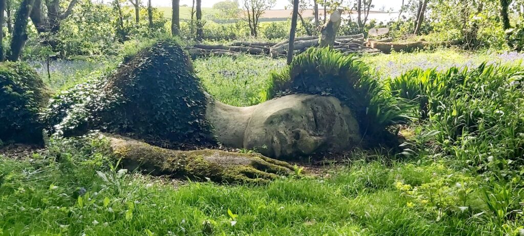 sculpture of a sleeping woman in the ground in a woodland at Heligan Gardens