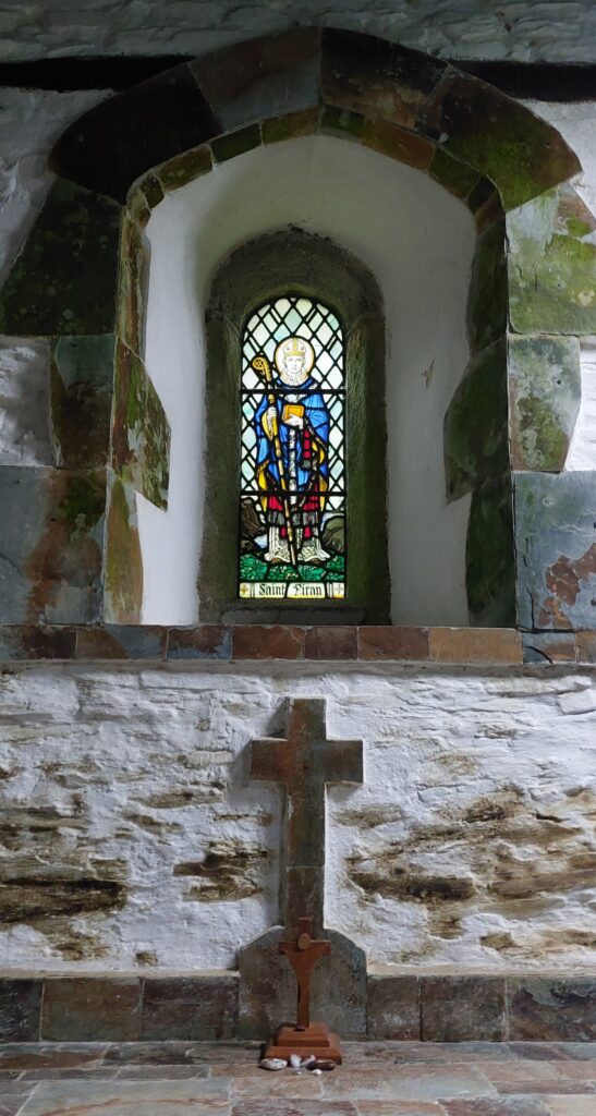 Stain glass window of St Piran including wooden cross in foreground